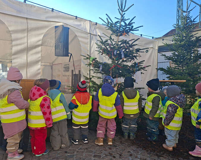Kinder mit gelben Westen von hinten vor dem Weihnachtsbaum