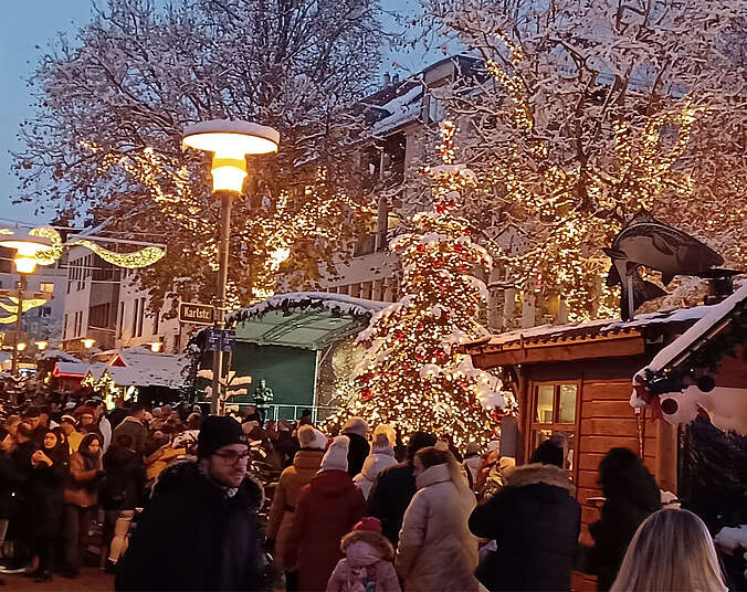 Erleuchtete Bäume mit Schnee bedeckt und Menschen auf dem Weihnachtsmarkt