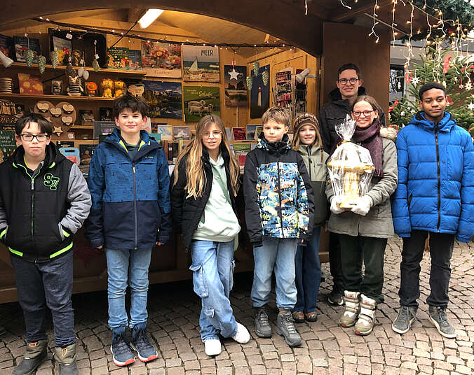 Kinder stehen vor der Weihnachtshütte. Eine Frau hält den goldenen Zeppelin-Jungen in der Hand.